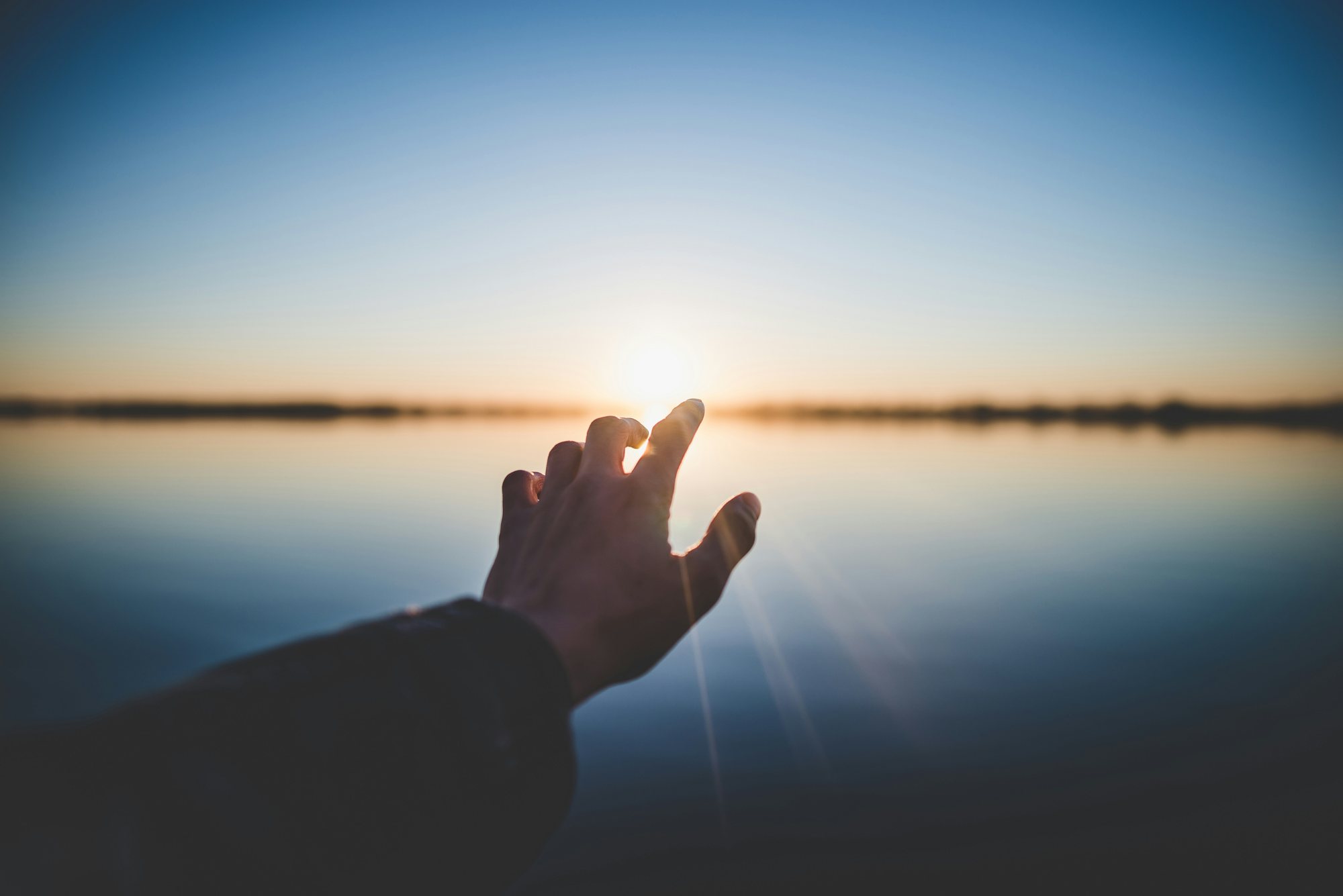 A hand reaching toward the sunrise, representing ongoing recovery